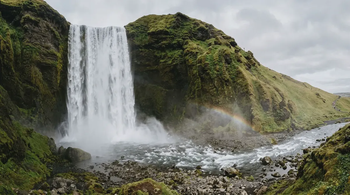 Skógafoss waterfall dropping over a mossy cliff in south Iceland with a faint rainbow in the spray